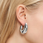 Nahaufnahme eines Frauenohrs mit nach hinten gestecktem blondem Haar, das LIEBESKIND BERLIN Creole - Organic Shapes von Liebeskind Berlin trägt: klobige, glänzende Creolen als perfekter minimalistischer Schmuck für einen eleganten Schmuck-Look.