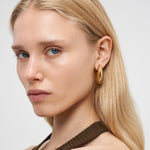 Frau mit langen blonden Haaren, die LIEBESKIND BERLIN Creole - Organic Shapes Ohrringe von Liebeskind Berlin und ein braunes Oberteil trägt, blickt in die Kamera und zeigt einen perfekten minimalistischen Stil.