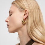 Frau mit langem blondem Haar trägt LIEBESKIND BERLIN Creole - Organic Shapes Goldohrringe von Liebeskind Berlin, dargestellt im Profil vor einem hellen Hintergrund.