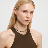 Frau mit langen blonden Haaren, die ein braunes Neckholder-Top, Goldschmuck und die LIEBESKIND BERLIN Halskette - Plates by Liebeskind Berlin trägt, schaut in die Kamera.