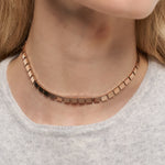 Eine Nahaufnahme einer Frau, die die Liebeskind Berlin Halskette - Plates trägt, elegant gestylt über einem hellgrauen Oberteil.