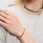 Eine Frau in einem hellgrauen Pullover trägt das LIEBESKIND BERLIN Armband - Plates von Liebeskind Berlin mit einem passenden Halsband - ideal für den urbanen Stil.