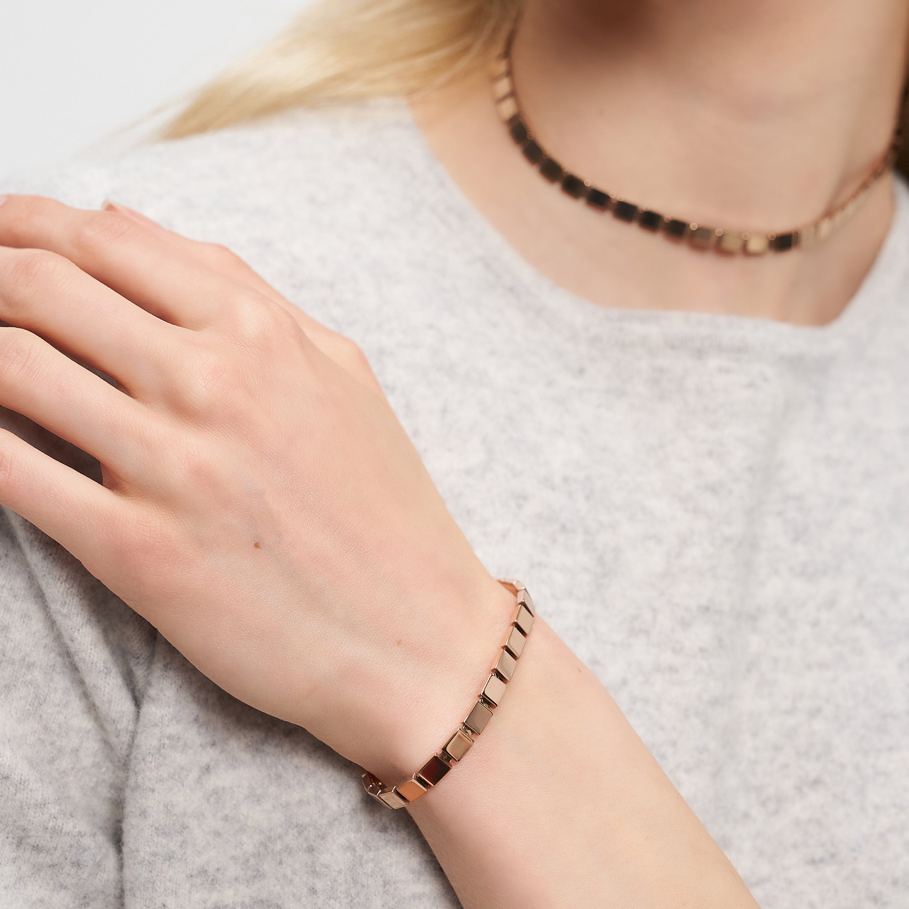 Eine Frau trägt einen urbanen Schmuck-Look mit einem goldenen Halsband und dem LIEBESKIND BERLIN Armband - Plates von Liebeskind Berlin, gestylt mit einem hellgrauen Pullover.