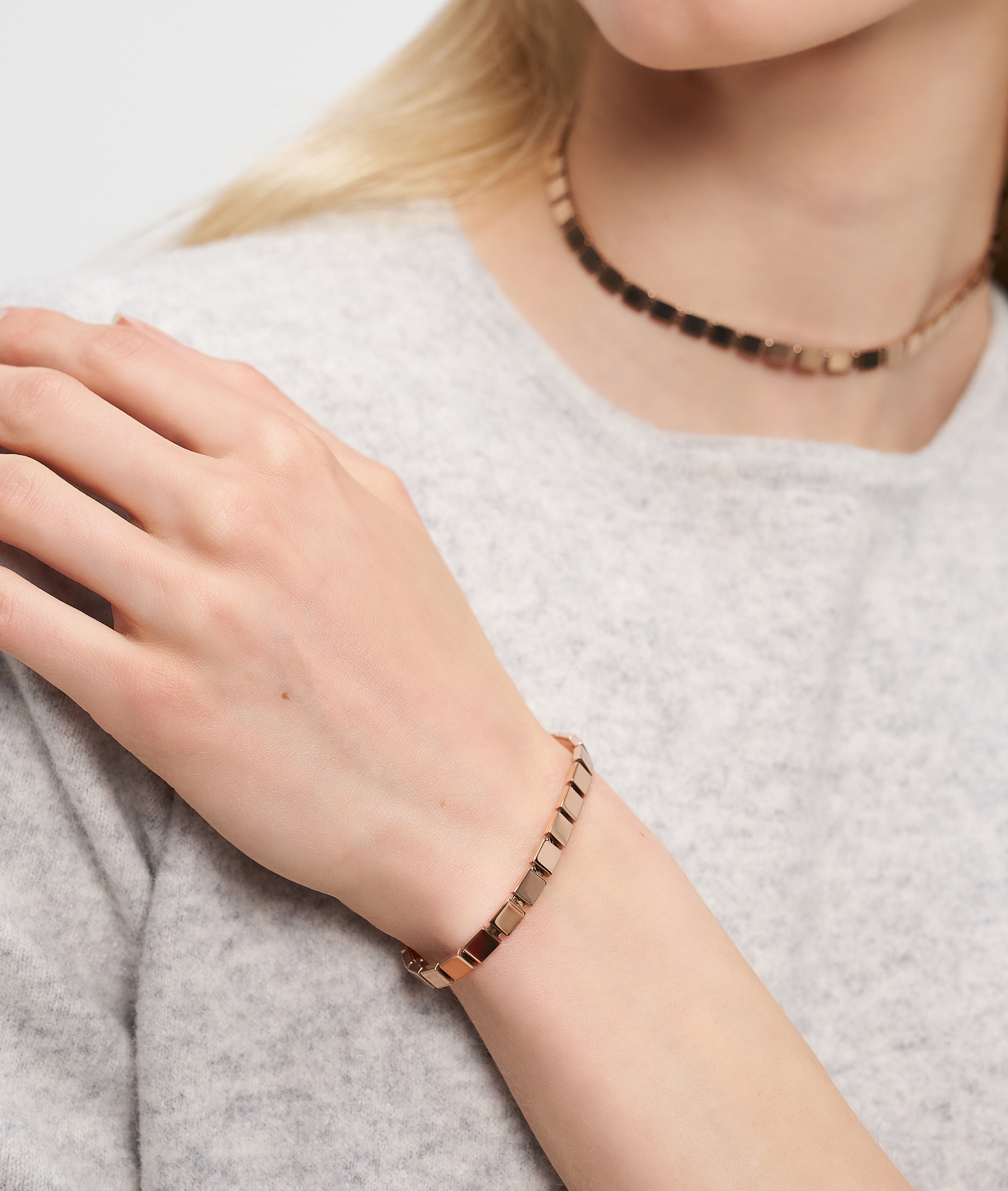 Eine Frau trägt einen urbanen Schmuck-Look mit einem goldenen Halsband und dem LIEBESKIND BERLIN Armband - Plates von Liebeskind Berlin, gestylt mit einem hellgrauen Pullover.