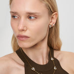 Frau im braunen Oberteil trägt LIEBESKIND BERLIN Ohrstecker - Glass Heart von Liebeskind Berlin und eine passende herzförmige Halskette, Blick zur Seite.