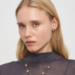 Eine Frau mit langen blonden Haaren trägt ein durchsichtiges graues Oberteil, einen Liebeskind Berlin Glass Heart Ohrstecker und eine passende Herz-Halskette.