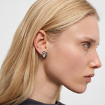 Eine Frau mit glattem blondem Haar trägt den Liebeskind Berlin Ohrstecker - Glass Heart, der im Profil vor einem schlichten Hintergrund gezeigt wird.