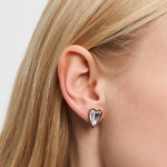 Nahaufnahme eines Frauenohrs mit dem Liebeskind Berlin Ohrstecker - Glass Heart mit silbernem Herzdesign und glattem blondem Haar.