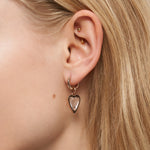 Nahaufnahme eines Frauenohrs mit LIEBESKIND BERLIN Creole - Glasherz-Ohrringen und zwei kleinen goldenen Ohrsteckern im oberen Ohr - Schmuck von Liebeskind Berlin.