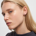 Eine blonde Frau, die ein dunkles Oberteil und Liebeskind Berlin Ohrstecker - Glass Heart trägt, schaut in die Kamera.