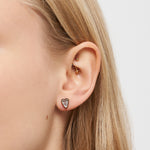 Nahaufnahme eines Frauenohrs mit zwei goldenen Helix-Piercings und einem Liebeskind Berlin Ohrstecker - Glass Heart im Ohrläppchen.