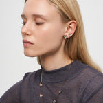 Frau mit geschlossenen Augen trägt LIEBESKIND BERLIN Ohrstecker - Glass Heart von Liebeskind Berlin und eine passende Halskette, gestylt mit einem grauen Top.