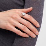 Eine Hand, die den Liebeskind Berlin Ring - Glass Heart mit modernem Design trägt, ruht auf einem lilafarbenen langärmeligen Top.