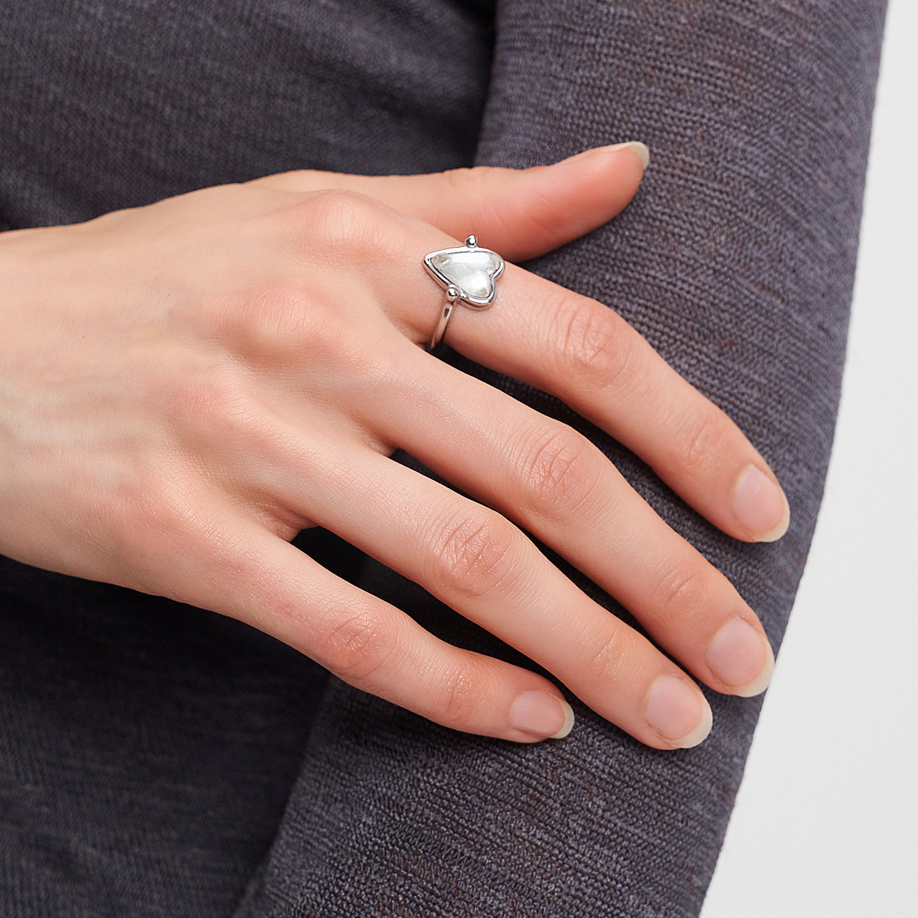 Eine Hand mit dem LIEBESKIND BERLIN Ring - Glass Heart von Liebeskind Berlin ruht auf einem lila Langarmtop - ein stilvoller Schmuck-Akzent für jedes Outfit.