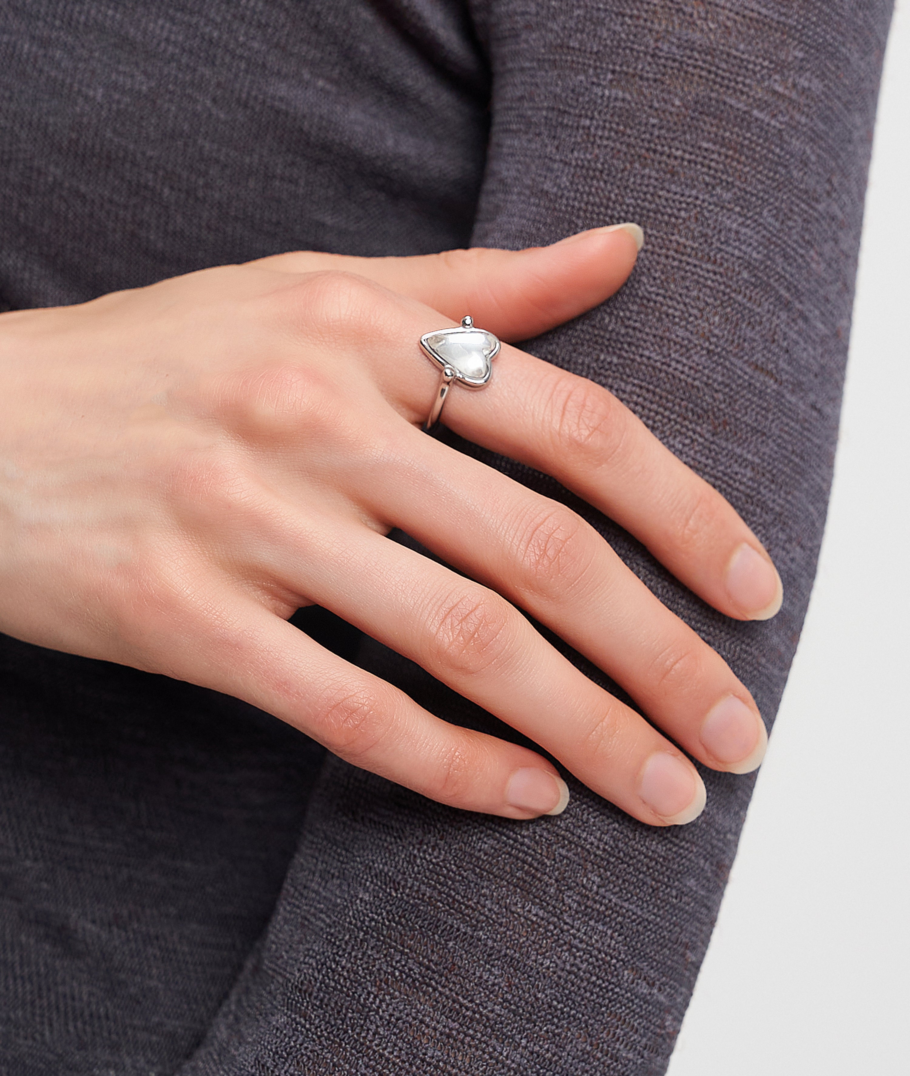 Eine Hand mit dem LIEBESKIND BERLIN Ring - Glass Heart von Liebeskind Berlin ruht auf einem lila Langarmtop - ein stilvoller Schmuck-Akzent für jedes Outfit.