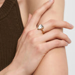 Eine Hand, die den Liebeskind Berlin Ring - Glass Heart mit Herzdetail trägt, ruht auf einem nackten Arm, gepaart mit einem braunen, ärmellosen Top - ein elegantes Accessoire als Mittelpunkt.