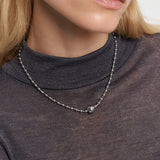 Frau trägt ein durchsichtiges, dunkles Oberteil und die LIEBESKIND BERLIN Halskette - Steel Ball von Liebeskind Berlin mit einer silbernen Perlenkette mit einem einzelnen runden Anhänger und Kugelverschluss für einen minimalistischen Look.