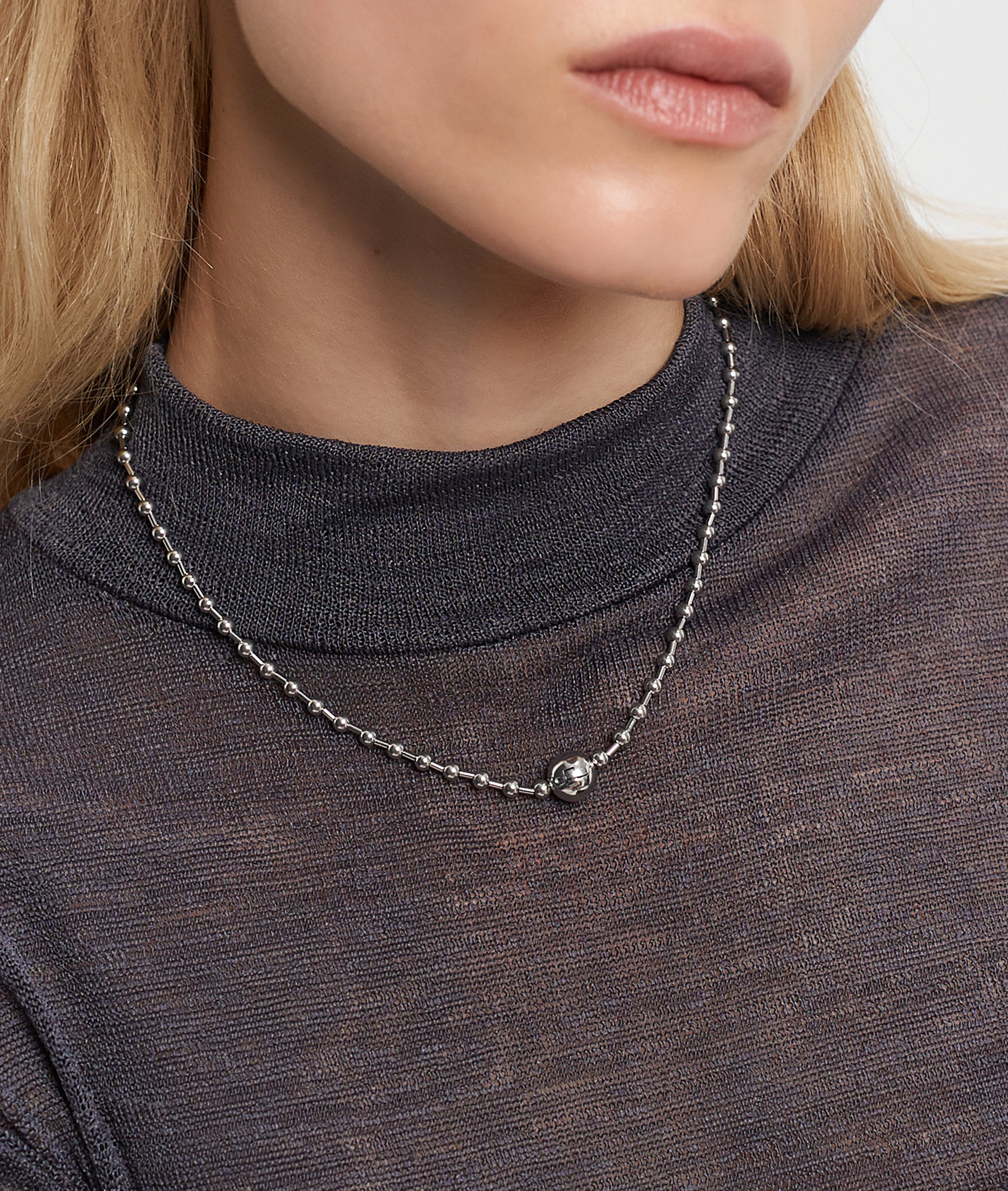 Frau trägt ein durchsichtiges, dunkles Oberteil und die LIEBESKIND BERLIN Halskette - Steel Ball von Liebeskind Berlin mit einer silbernen Perlenkette mit einem einzelnen runden Anhänger und Kugelverschluss für einen minimalistischen Look.