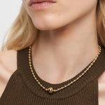 Frau trägt die Liebeskind Berlin Halskette - Steel Ball, eine minimalistische Goldperlenkette, gepaart mit einem braunen ärmellosen Oberteil, von den Schultern bis zum Kinn gezeigt.