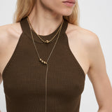 Frau trägt ein geripptes braunes Halstertop und mehrere goldene Halsketten, darunter die Liebeskind Berlin Halskette - Steel Ball mit ihrem minimalistischen Design und dezenten Perlenakzenten.
