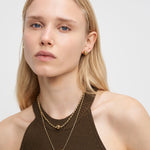 Eine Frau mit langen blonden Haaren trägt ein braunes Neckholder-Top, goldene Ohrringe und die Liebeskind Berlin Halskette - Steel Ball.