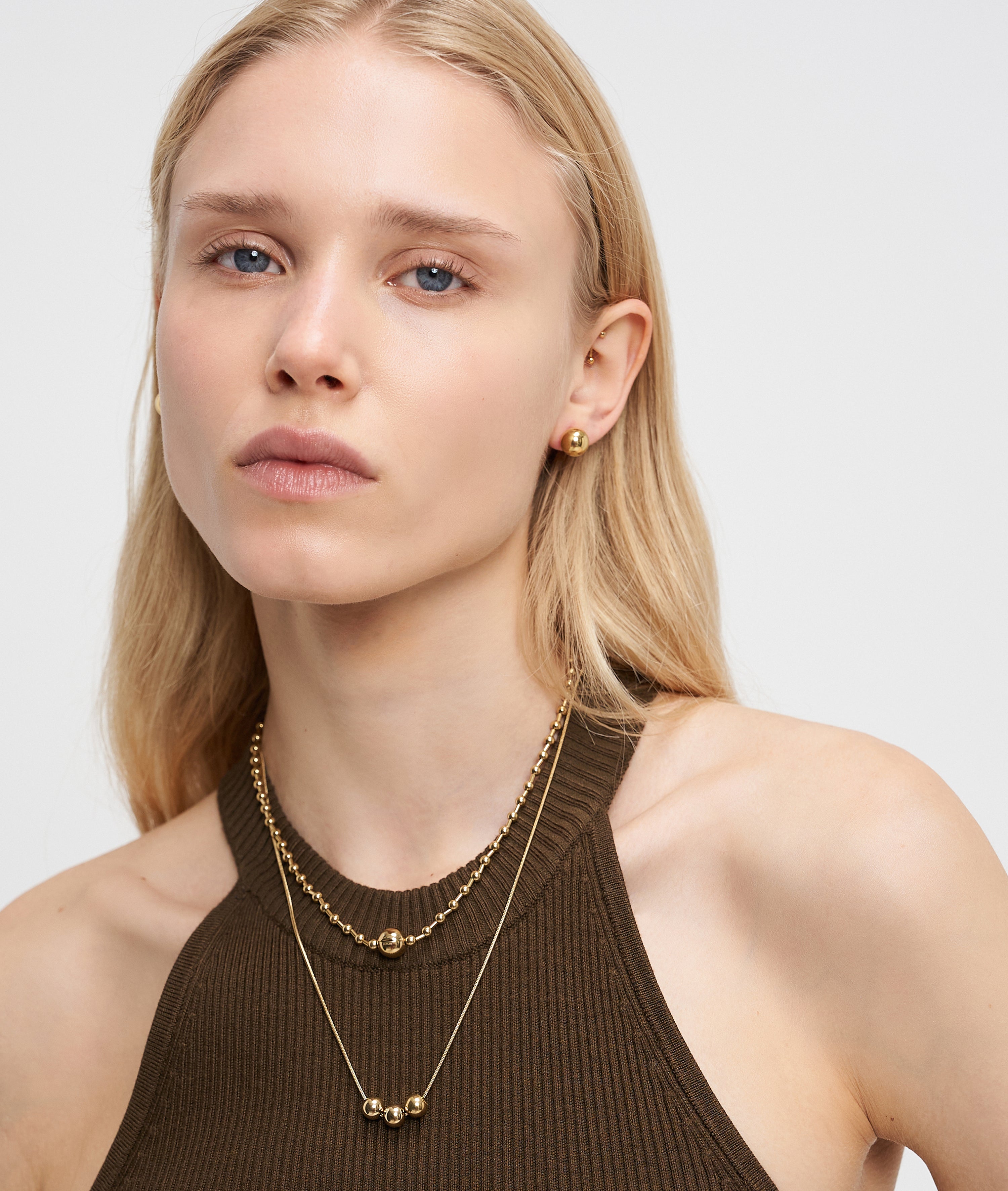 Eine Frau mit langen blonden Haaren trägt ein braunes Neckholder-Top, goldene Ohrringe und die Liebeskind Berlin Halskette - Steel Ball.