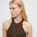 Eine Frau mit langen blonden Haaren trägt ein braunes ärmelloses Oberteil und die LIEBESKIND BERLIN Halskette - Steel Ball von Liebeskind Berlin in Gold und schaut zur Seite.