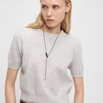 Frau in einem hellgrauen, kurzärmeligen Pullover und einer schwarzen Lederhose, gestylt mit der Liebeskind Berlin Halskette - Steel Ball für einen eleganten, minimalistischen Look.