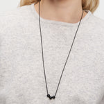 Eine Frau trägt eine Liebeskind Berlin Halskette - Steel Ball mit drei schwarzen Perlen über einem hellgrauen Pullover, wodurch das minimalistische Design hervorgehoben wird.