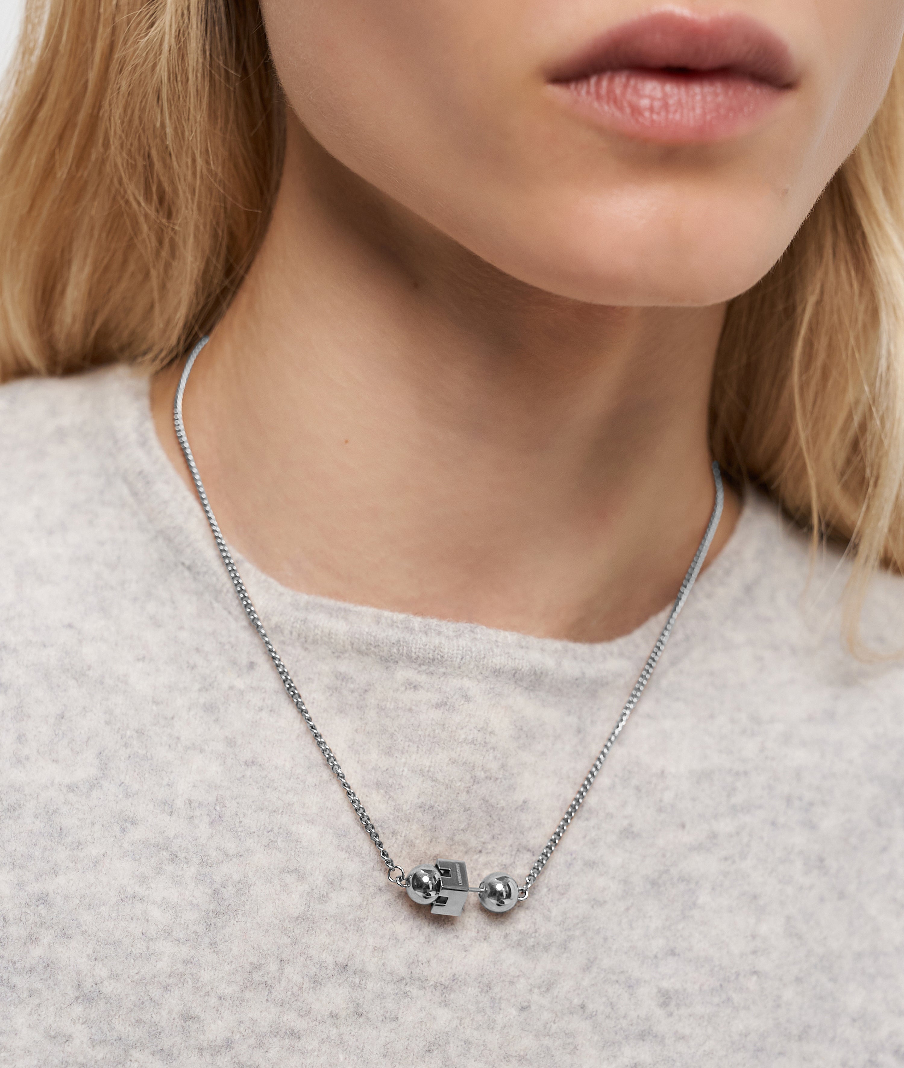 Eine Frau von den Schultern aufwärts trägt die Liebeskind Berlin Halskette - Steel Ball, mit geometrischen und kugelförmigen Anhängern, die das minimalistische Design unterstreichen.