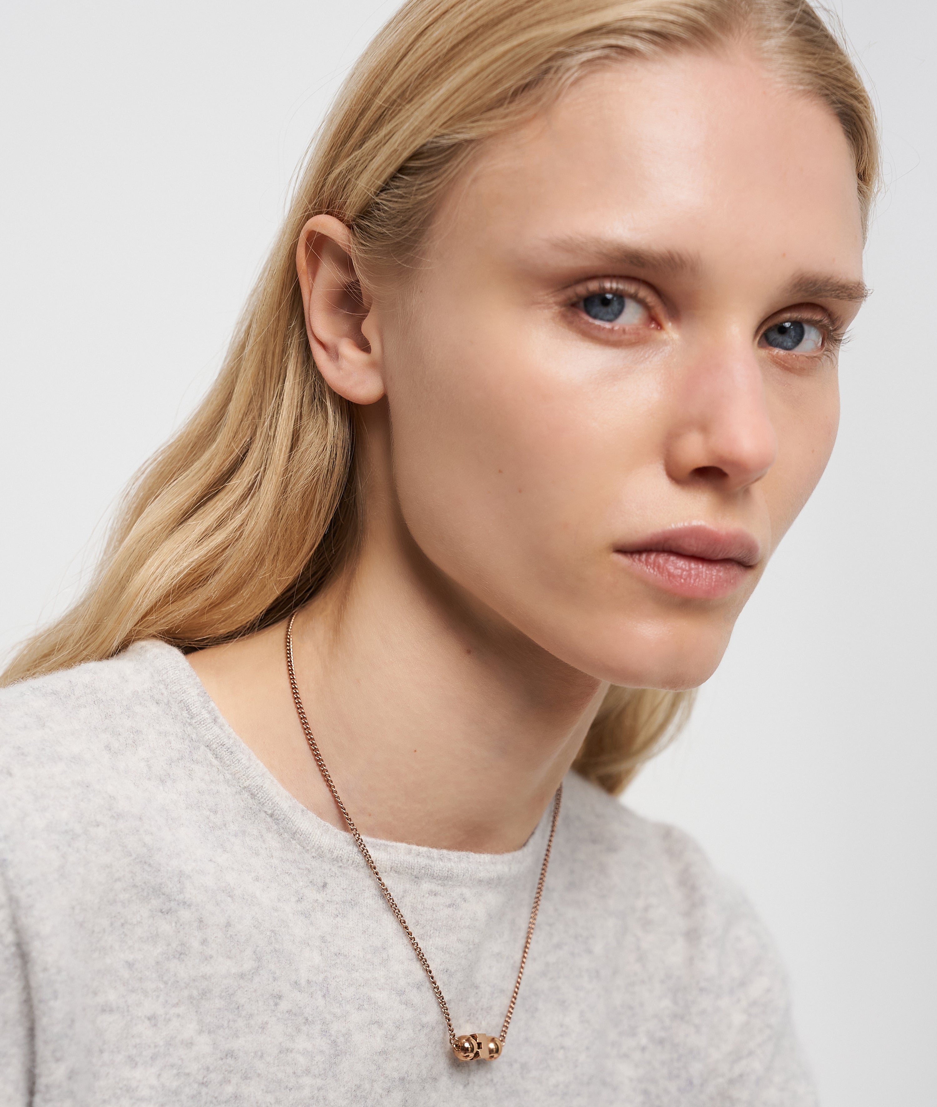 Eine Frau mit langen blonden Haaren und einem hellen Pullover trägt die LIEBESKIND BERLIN Halskette - Steel Ball von Liebeskind Berlin in einem minimalistischen Design und schaut leicht zur Seite.