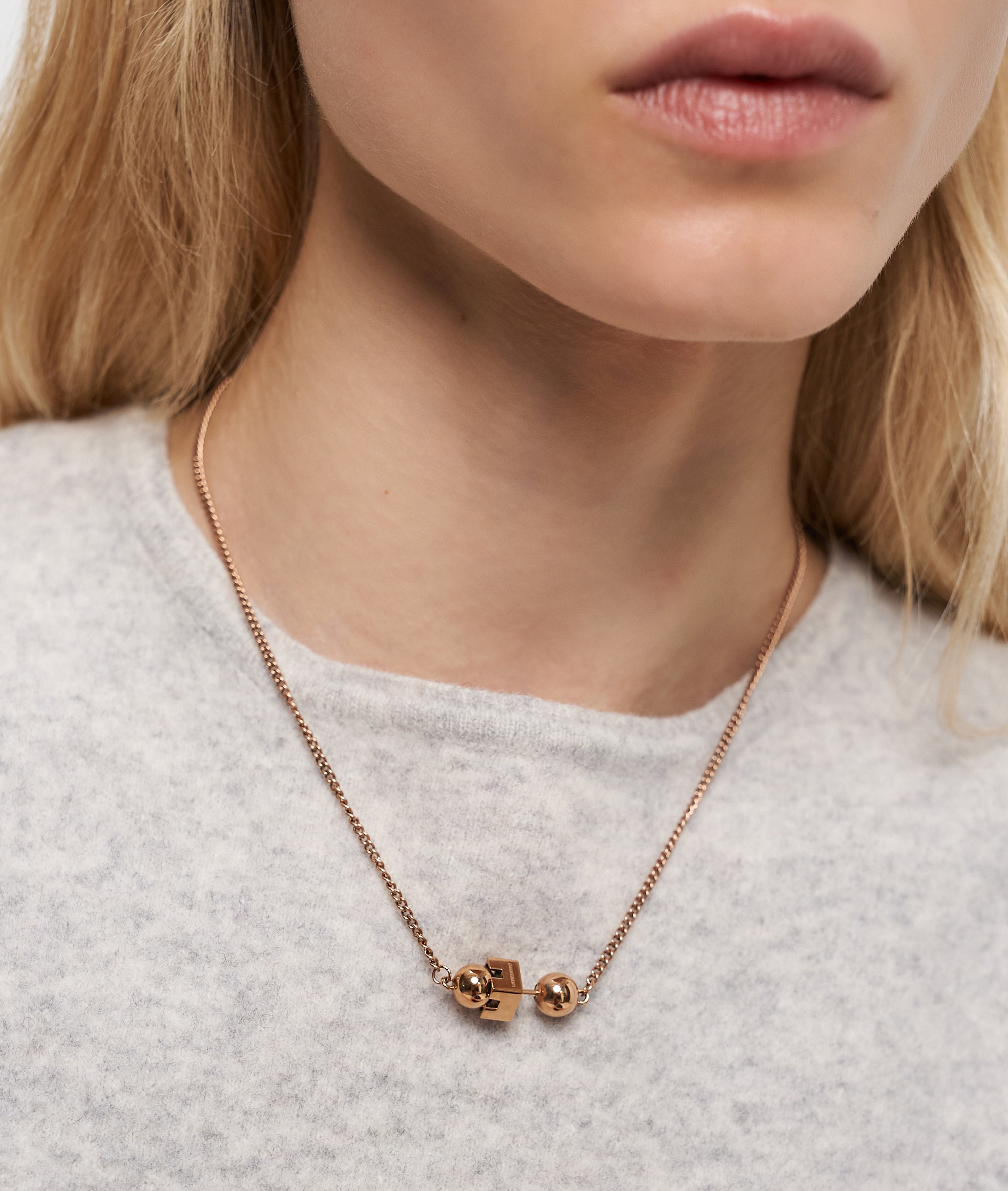 Eine Frau trägt die Liebeskind Berlin Halskette - Steel Ball über einem leichten Pullover und hebt das elegante, minimalistische Design mit geometrischen und kugelförmigen Anhängern hervor.