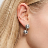 Nahaufnahme einer Person, die den Liebeskind Berlin Ohrstecker - Steel Ball trägt und ihr glattes blondes Haar ordentlich hinter das Ohr gesteckt hat.