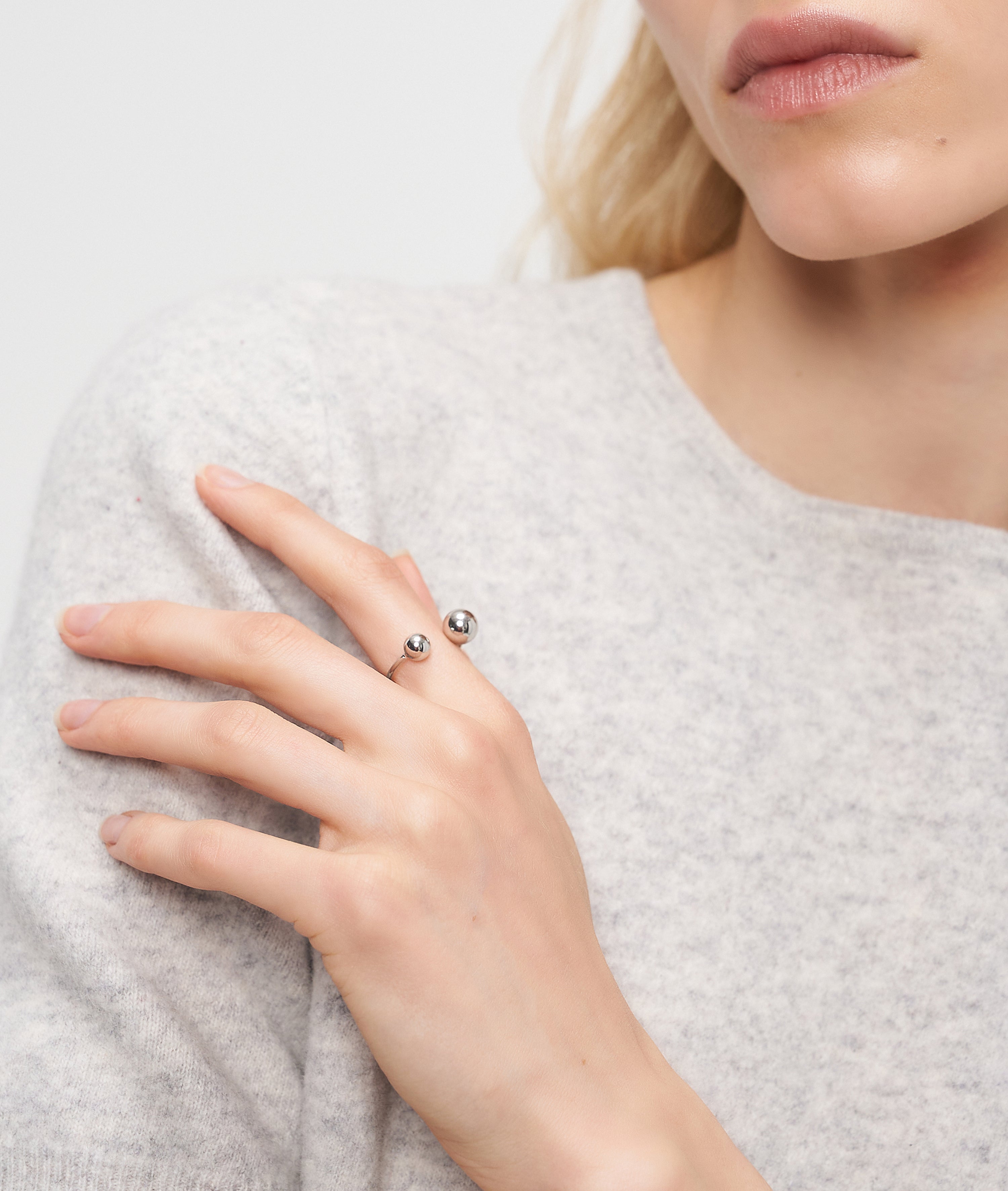 Eine Frau in einem hellgrauen Pullover berührt ihre Brust, während sie den Liebeskind Berlin Steel Ball Ring trägt.