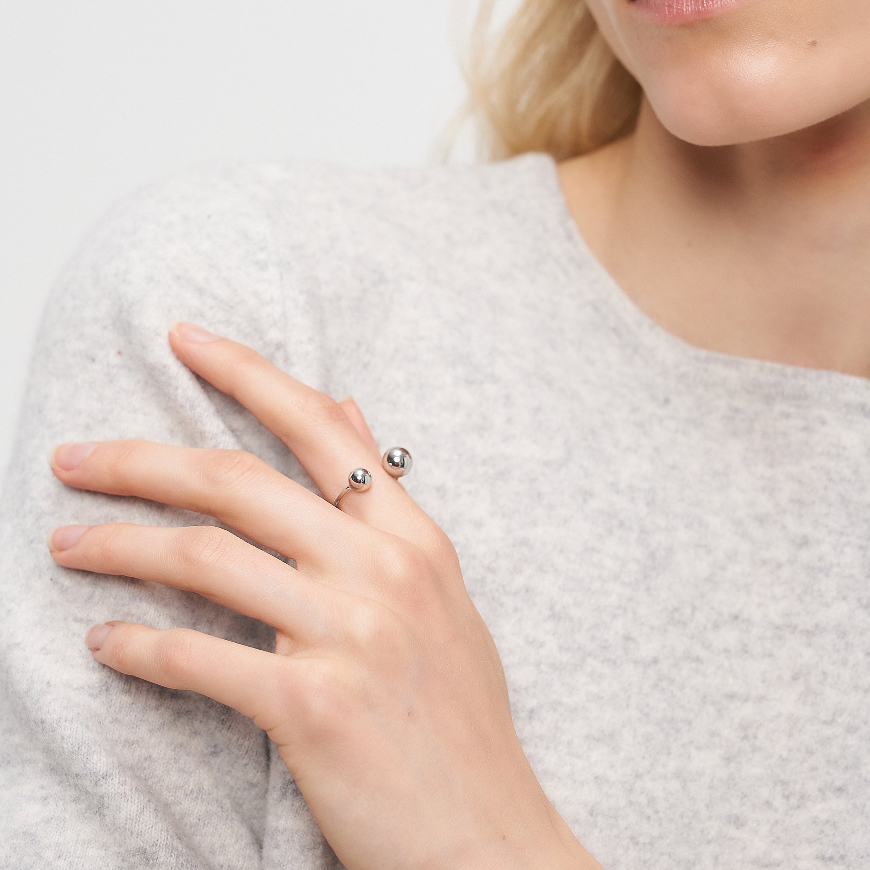 Frau trägt einen leichten Pullover und den minimalistischen LIEBESKIND BERLIN Ring - Steel Ball von Liebeskind Berlin, einen modernen, eleganten, offenen Ring mit zwei Kugeln - perfekt für jede Gelegenheit.
