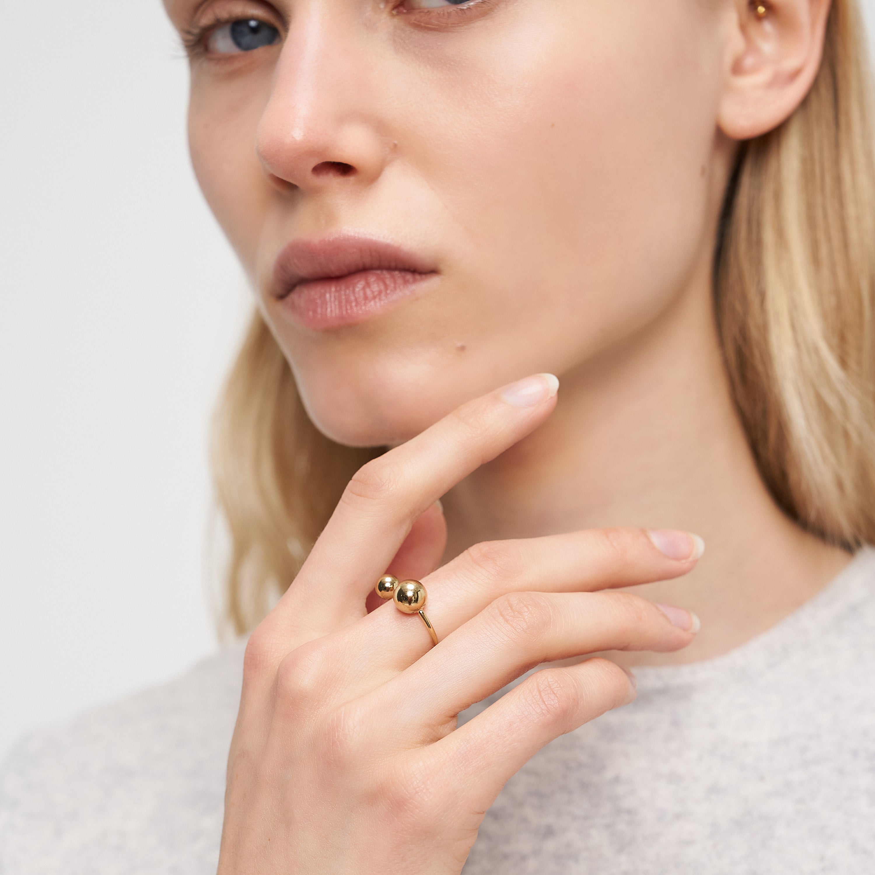 Eine blonde Frau, die einen Liebeskind Berlin Ring - Steel Ball und ein Nasenpiercing trägt, berührt ihr Gesicht und blickt in die Kamera, wobei sie modernes Designflair präsentiert.