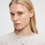 Eine Frau mit langen blonden Haaren in einem hellen Top trägt die Liebeskind Berlin Halskette - Organic Shapes und Ohrstecker und schaut in die Kamera.