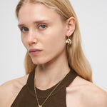 Frau mit langen blonden Haaren trägt eine LIEBESKIND BERLIN Halskette - Organic Shapes von Liebeskind Berlin, gepaart mit goldenem Schmuck, stilvollen goldenen Ohrringen und einem ärmellosen braunen Top.