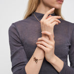 Frau in einem grauen Oberteil trägt goldenen Schmuck, darunter das Liebeskind Berlin Armband - Organic Shapes, gepaart mit einer zarten Halskette und Ohrringen.