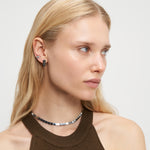 Frau mit langen blonden Haaren trägt ein braunes ärmelloses Oberteil und minimalistische Liebeskind Berlin Ohrring - Plates Ohrringe mit einem Kropfband.