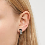 Nahaufnahme eines Frauenohrs mit zwei goldenen Ohrsteckern und einem rechteckigen schwarzen Creolenohrring, die das minimalistische Design des Liebeskind Berlin Ohrring - Plates unterstreichen.