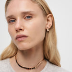 Frau mit glattem blondem Haar trägt einen goldenen Liebeskind Berlin Ohrring - Plates und eine Halskette, schaut mit neutralem Blick in die Kamera und setzt auf minimalistisches Design.