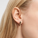 Nahaufnahme eines Frauenohrs mit glattem blondem Haar, das den Liebeskind Berlin Ohrring - Plates trägt, einen klobigen rechteckigen Ohrring aus Gold mit minimalistischem Design.