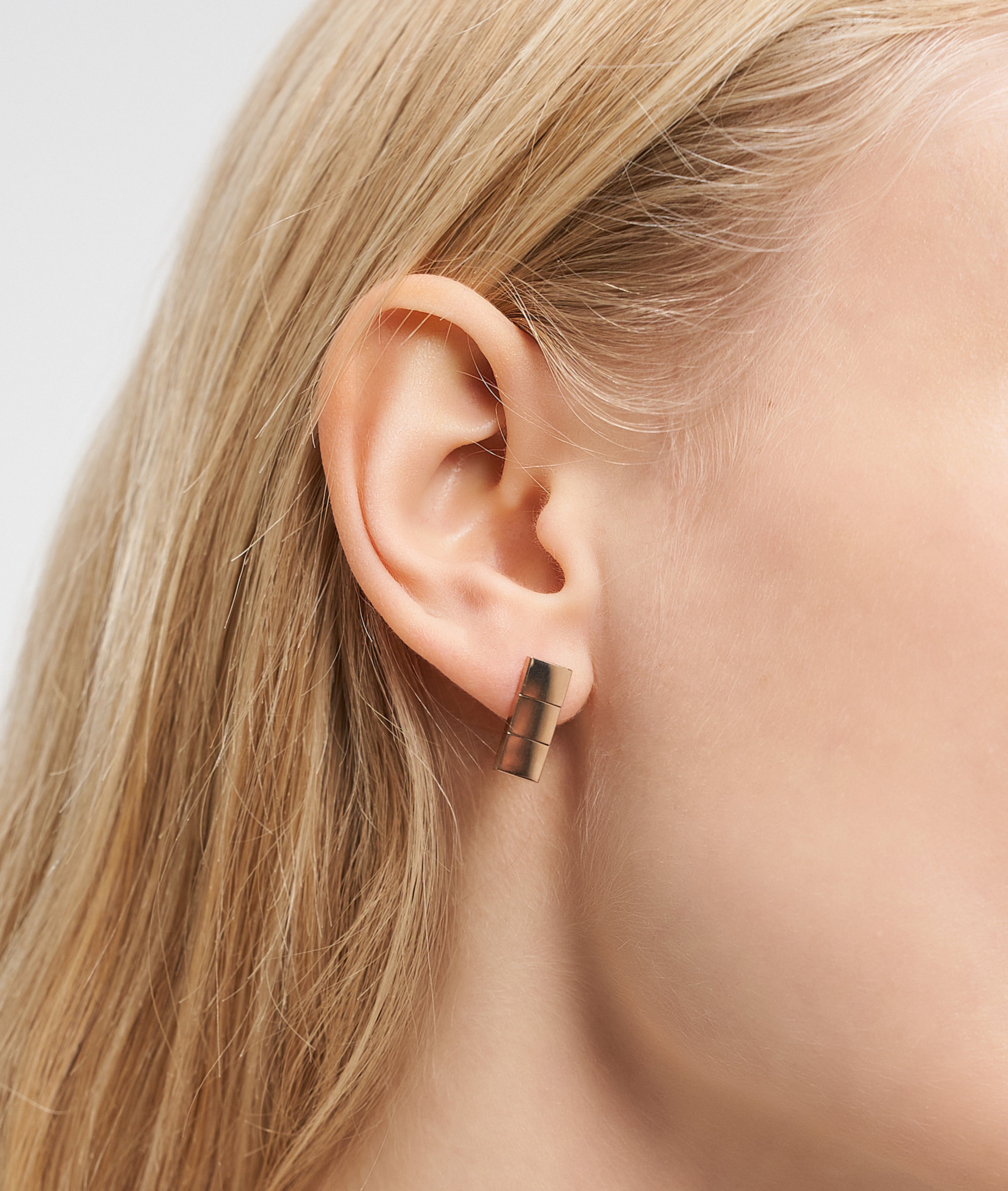 Nahaufnahme eines Frauenohrs mit glattem blondem Haar, das den Liebeskind Berlin Ohrring - Plates trägt, einen klobigen rechteckigen Ohrring aus Gold mit minimalistischem Design.