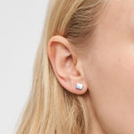 Nahaufnahme des Ohrs einer Person, die den Liebeskind Berlin Ohrring - Plates trägt, einen kleinen, rechteckigen Ohrring von Liebeskind Berlin - ein ideales Beispiel für minimalistischen Schmuck.