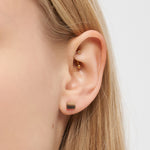 Nahaufnahme eines Frauenohrs mit minimalistischem Ohrstecker aus Gold und einem kleinen quadratischen Ohrstecker aus der Kollektion Liebeskind Berlin Ohrring - Plates von Liebeskind Berlin.