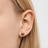 Nahaufnahme eines Frauenohrs mit minimalistischem Ohrstecker aus Gold und einem kleinen quadratischen Ohrstecker aus der Kollektion Liebeskind Berlin Ohrring - Plates von Liebeskind Berlin.