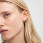 Nahaufnahme eines Frauengesichts mit blondem Haar, das Liebeskind Berlin Ohrring - My Heart Ohrringe und mehrere Ohrpiercings trägt.