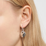 Nahaufnahme eines Frauenohrs mit goldenen Helix-Piercings und dem Liebeskind Berlin Ohrring - Organic Shapes, einem silbernen Ohrring in Herzform, der einen eleganten Akzent von Liebeskind Berlin setzt.