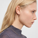 Eine Frau mit langen blonden Haaren trägt den Liebeskind Berlin Ohrring - Organic Shapes als modernes Accessoire zu einem grauen Oberteil, dargestellt im Profil vor weißem Hintergrund.